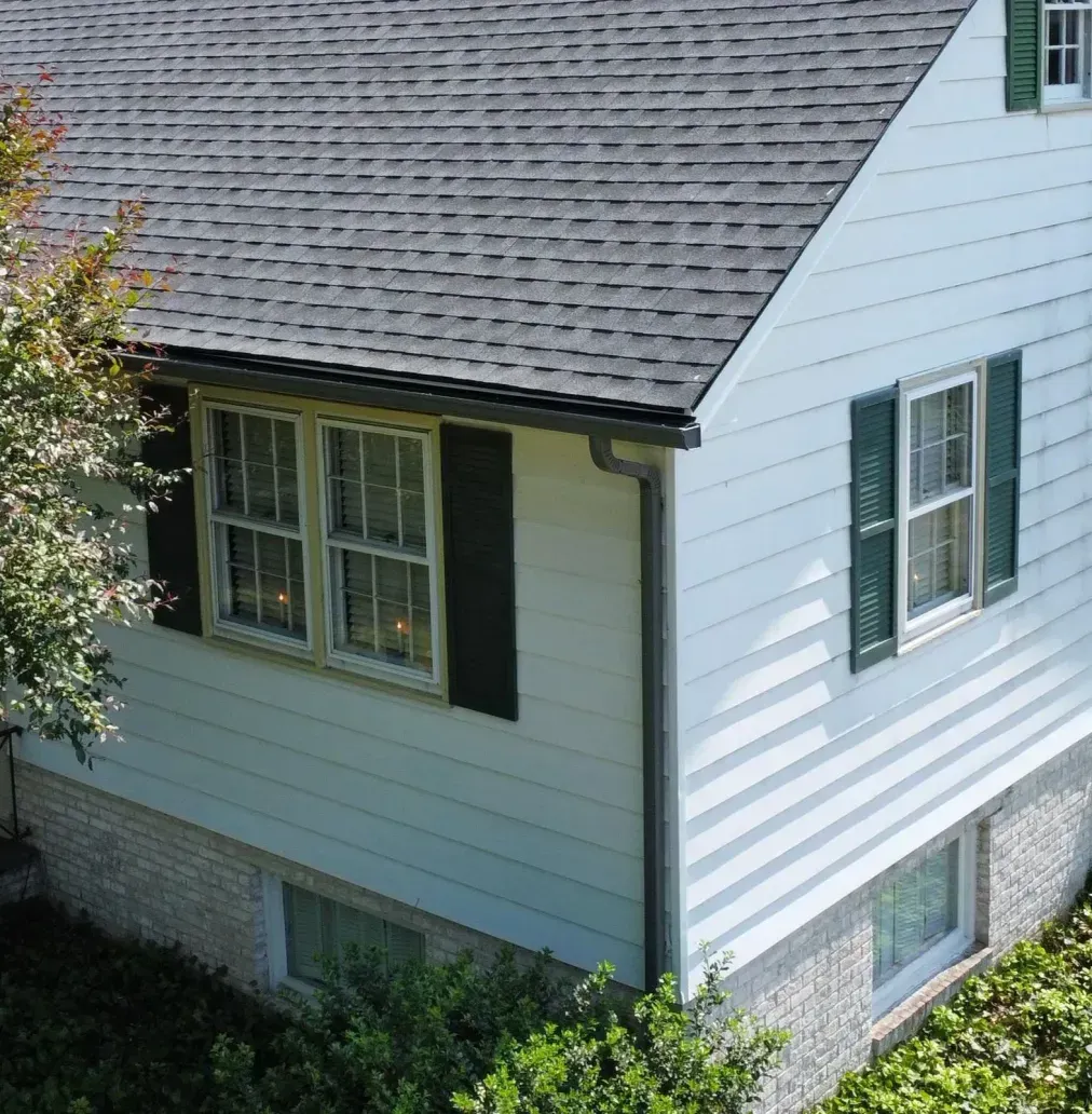White house exterior with gray roof, green shutters, and windows seen from the side yard