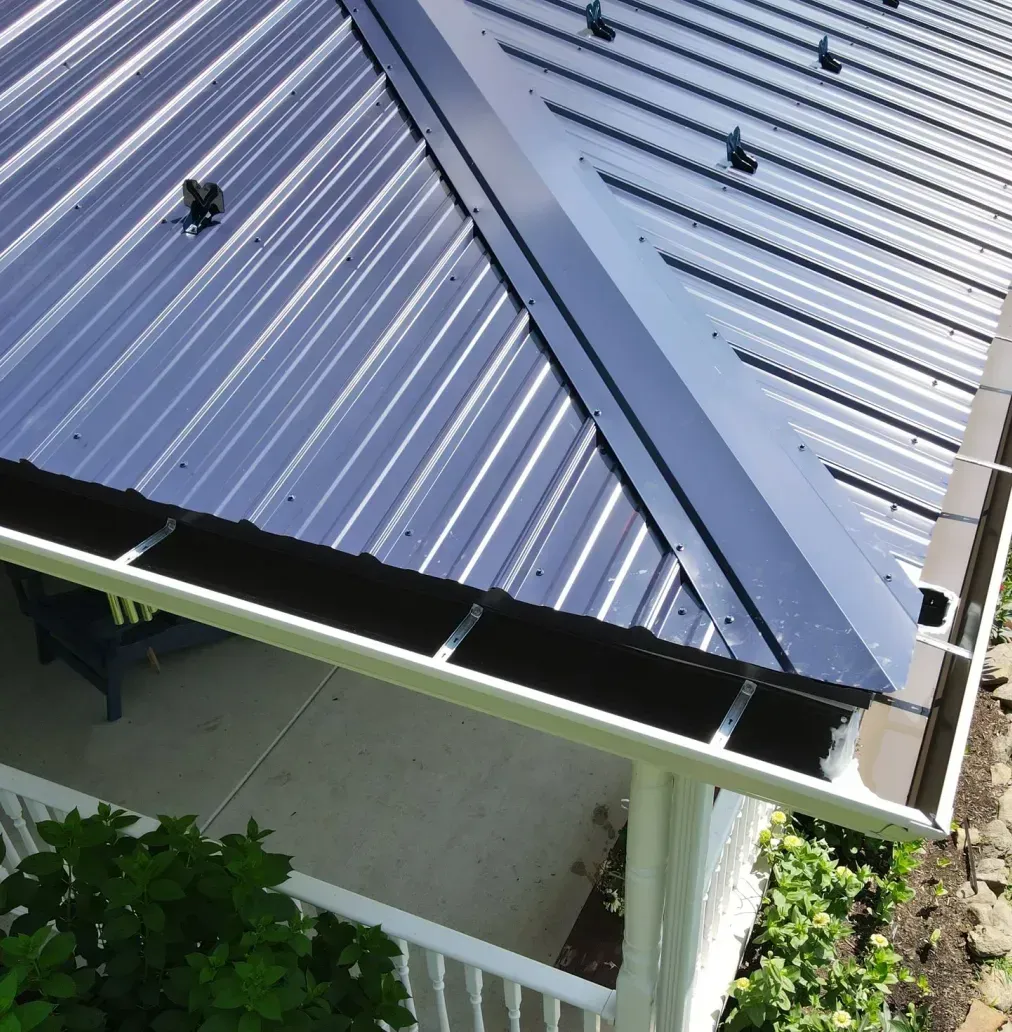 Blue metal roof over a covered patio with white beams and plants below