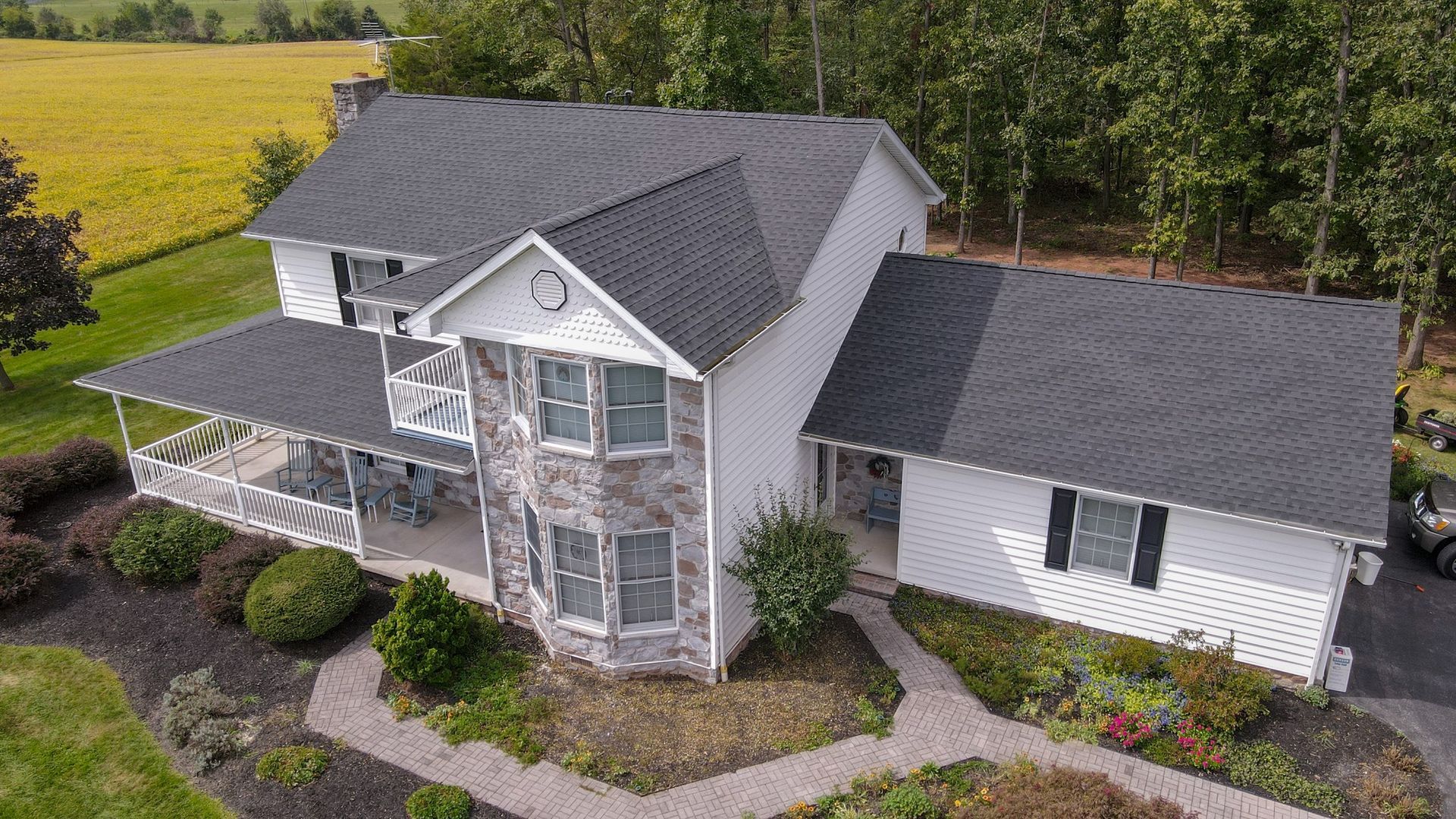 Aerial view of a white two-story suburban house with a gray roof, surrounded by landscaping and trees.