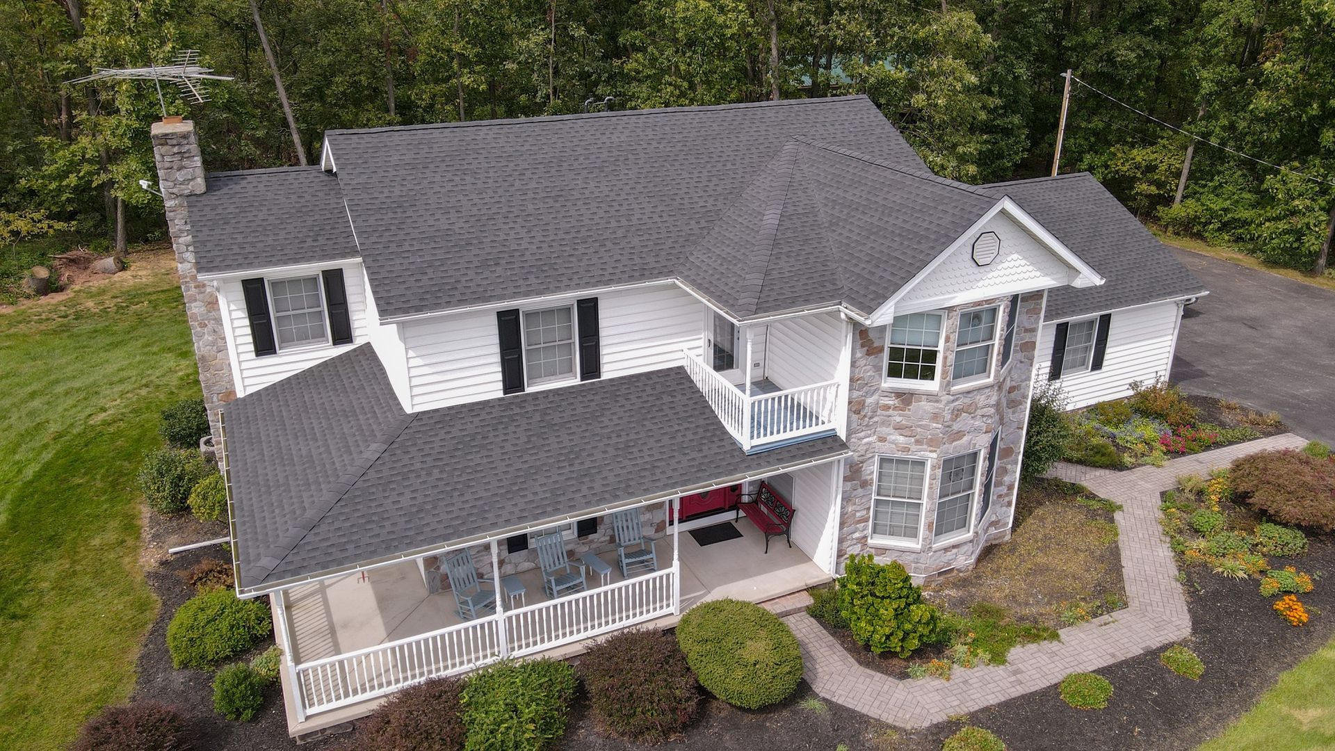 Aerial view of a large gray two-story house with white trim, a covered porch, and landscaped yard.