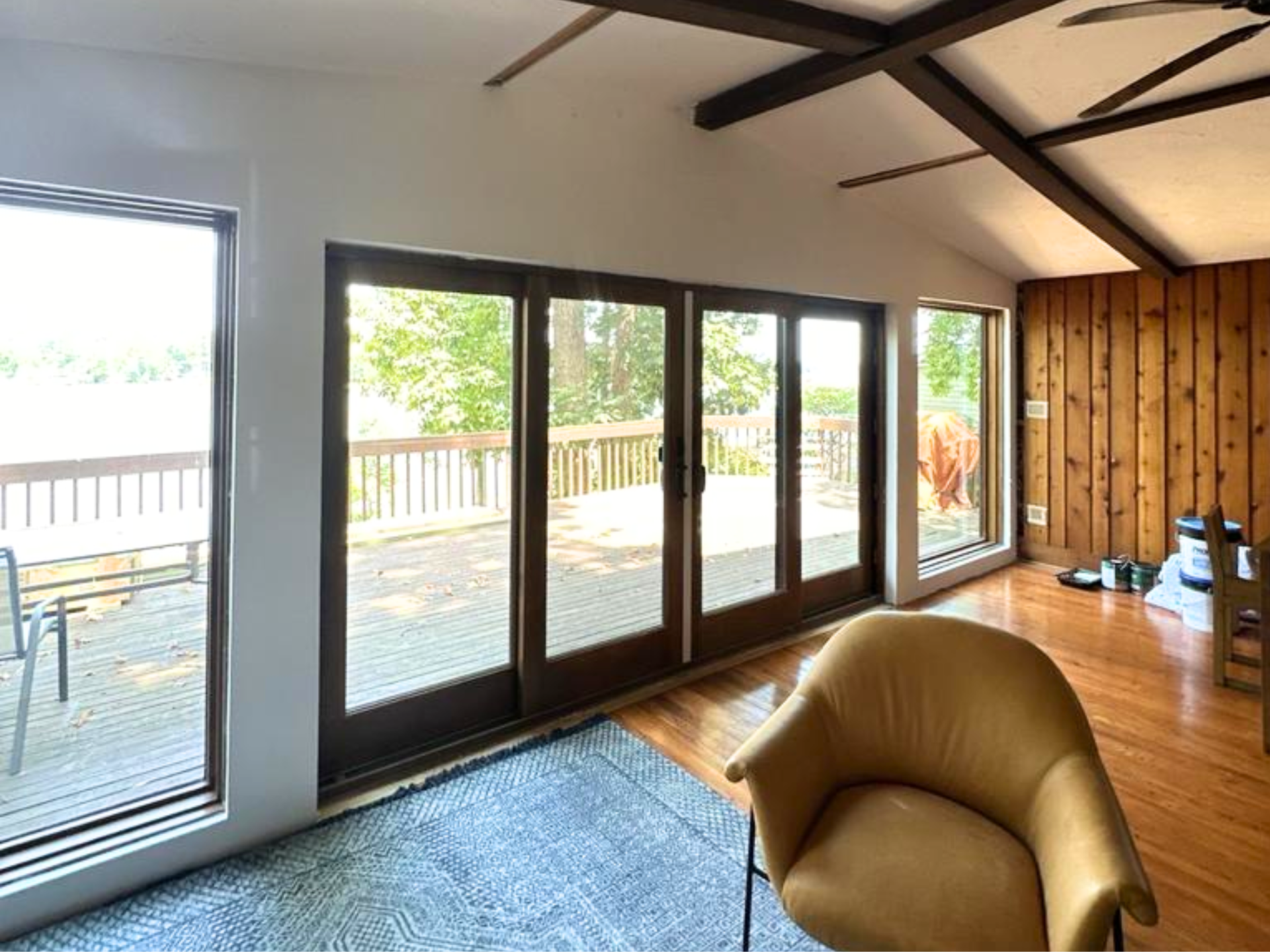 Modern living room with large glass doors, wood-paneled wall, vaulted ceiling, and tan chair