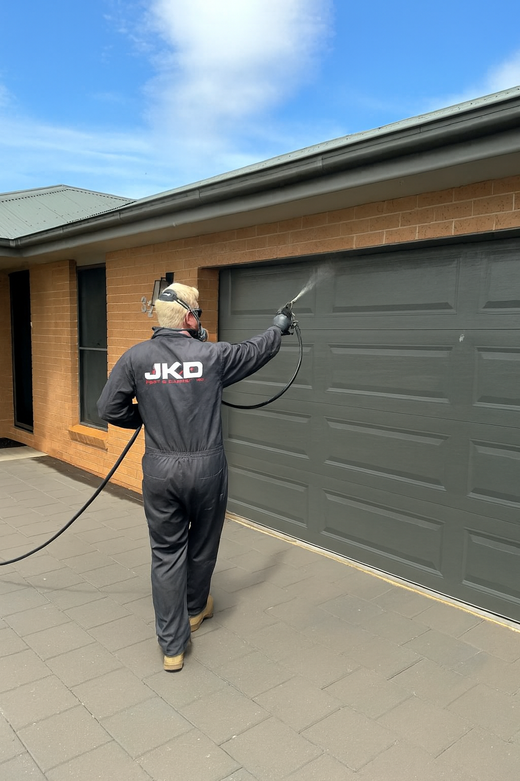 A Man is Spraying a Garage Door With a Sprayer — JKD Pest & Carpentry In Dubbo, NSW