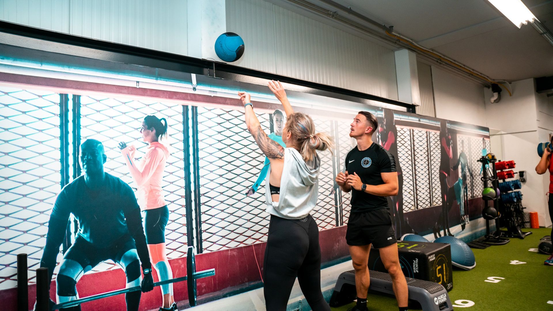 Een vrouw doet een fitness oefening met een medicine bal terwijl een personal trainer toekijkt.