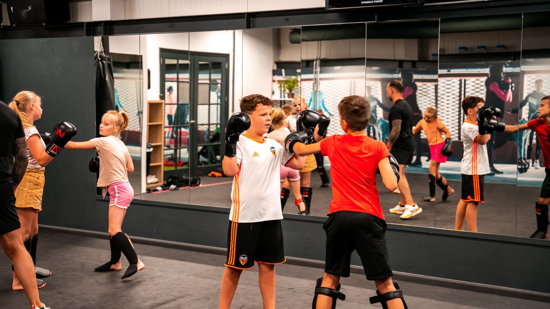 Een groep kinderen is aan het boksen in een sportschool voor een spiegel.