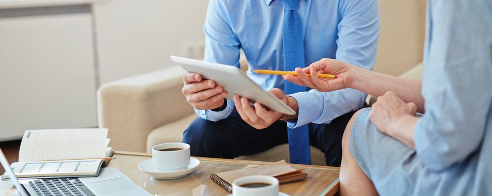 A man and a woman are sitting on a couch looking at a tablet.