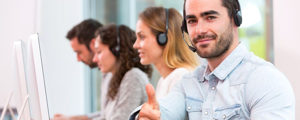 A group of people wearing headsets are sitting in front of computers in a call center.