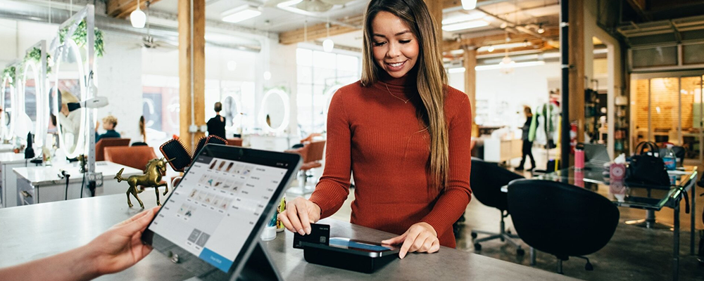 A woman is standing at a counter using a tablet.