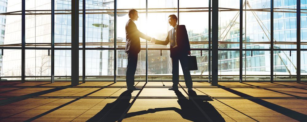 Two businessmen are shaking hands in front of a large window.
