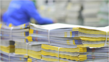 A man in a blue shirt is standing behind a stack of newspapers.