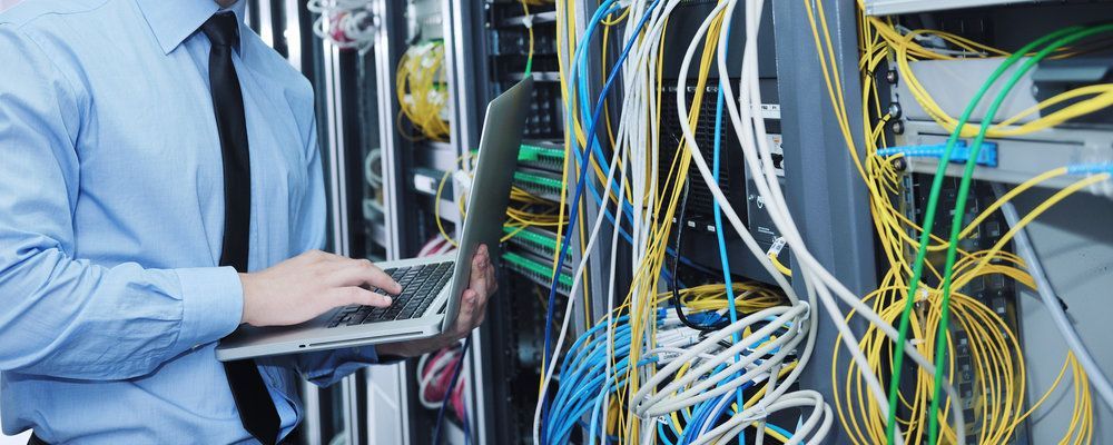A man is using a laptop computer in a server room.