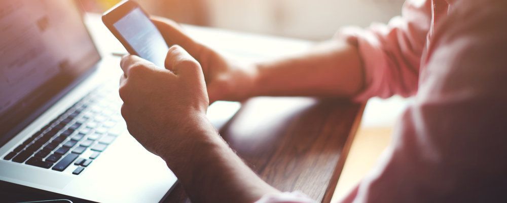 A person is sitting at a table using a laptop and a cell phone.