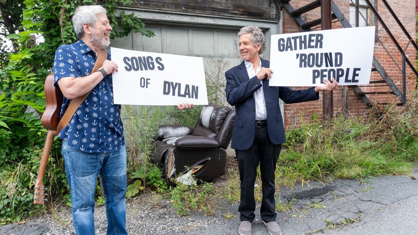 Kenny Butler and Steve Alves holding signs reading Songs of Dylan and Gather 'Round People