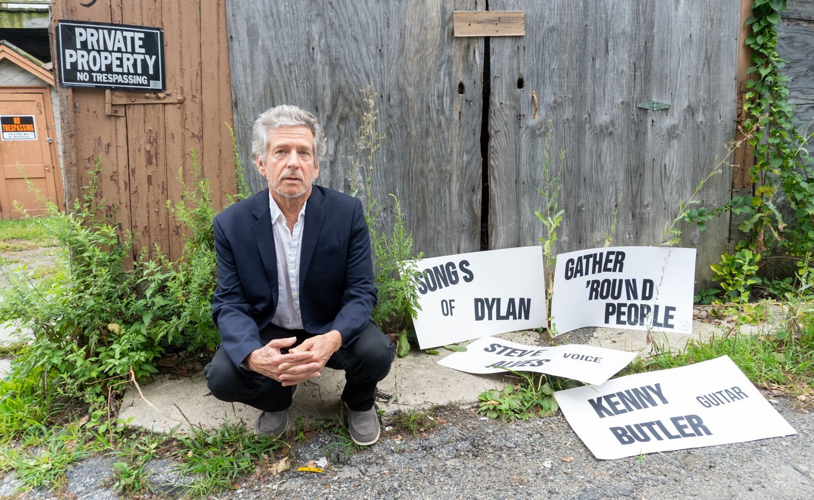 Steve Alves crouching in front of a weathered wooden door