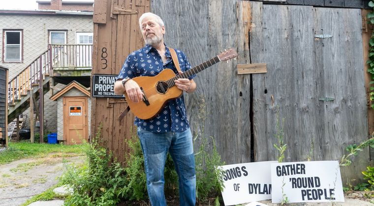 Kenny Butler playing guitar in front of a weathered wooden door