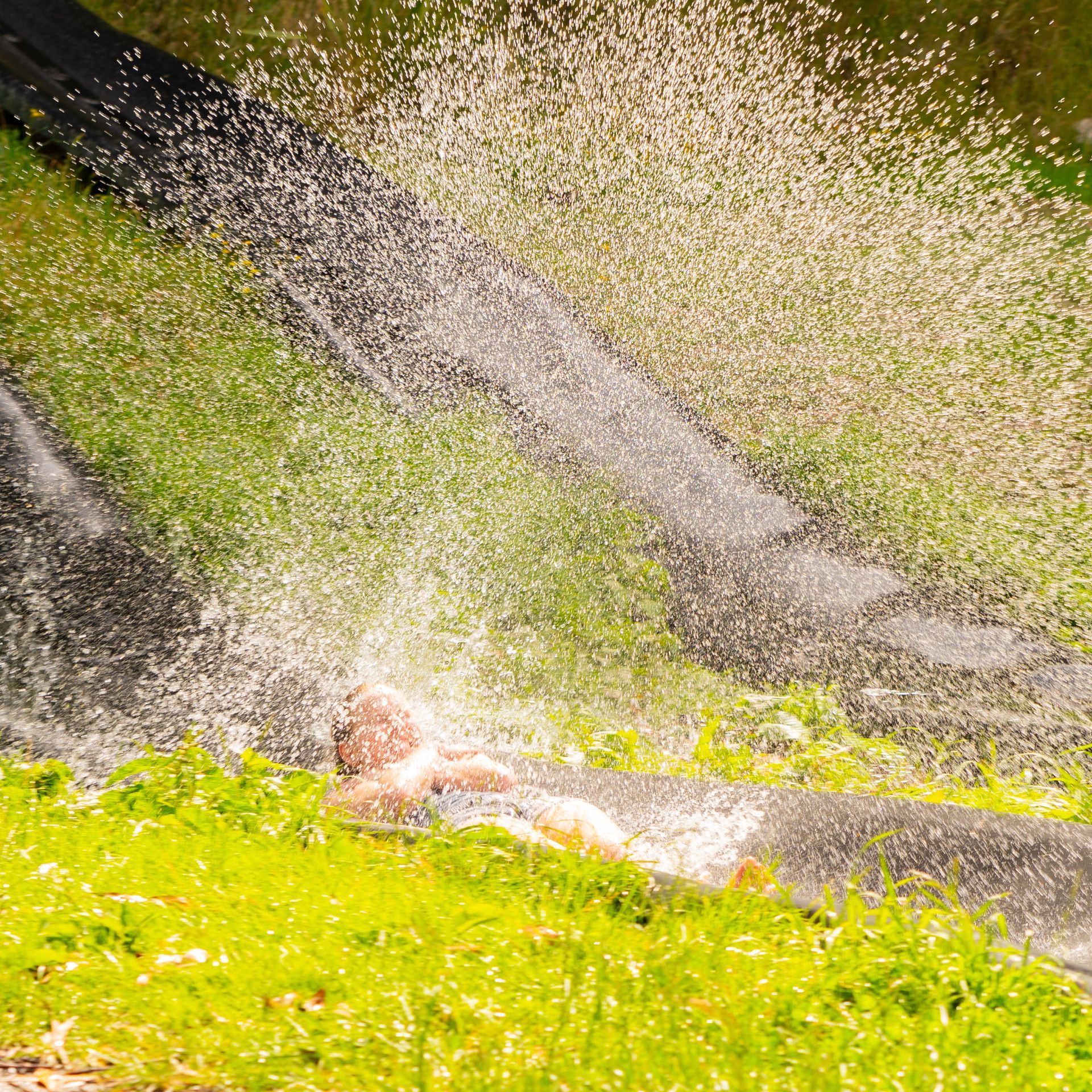 A person is laying in the grass under a waterfall.