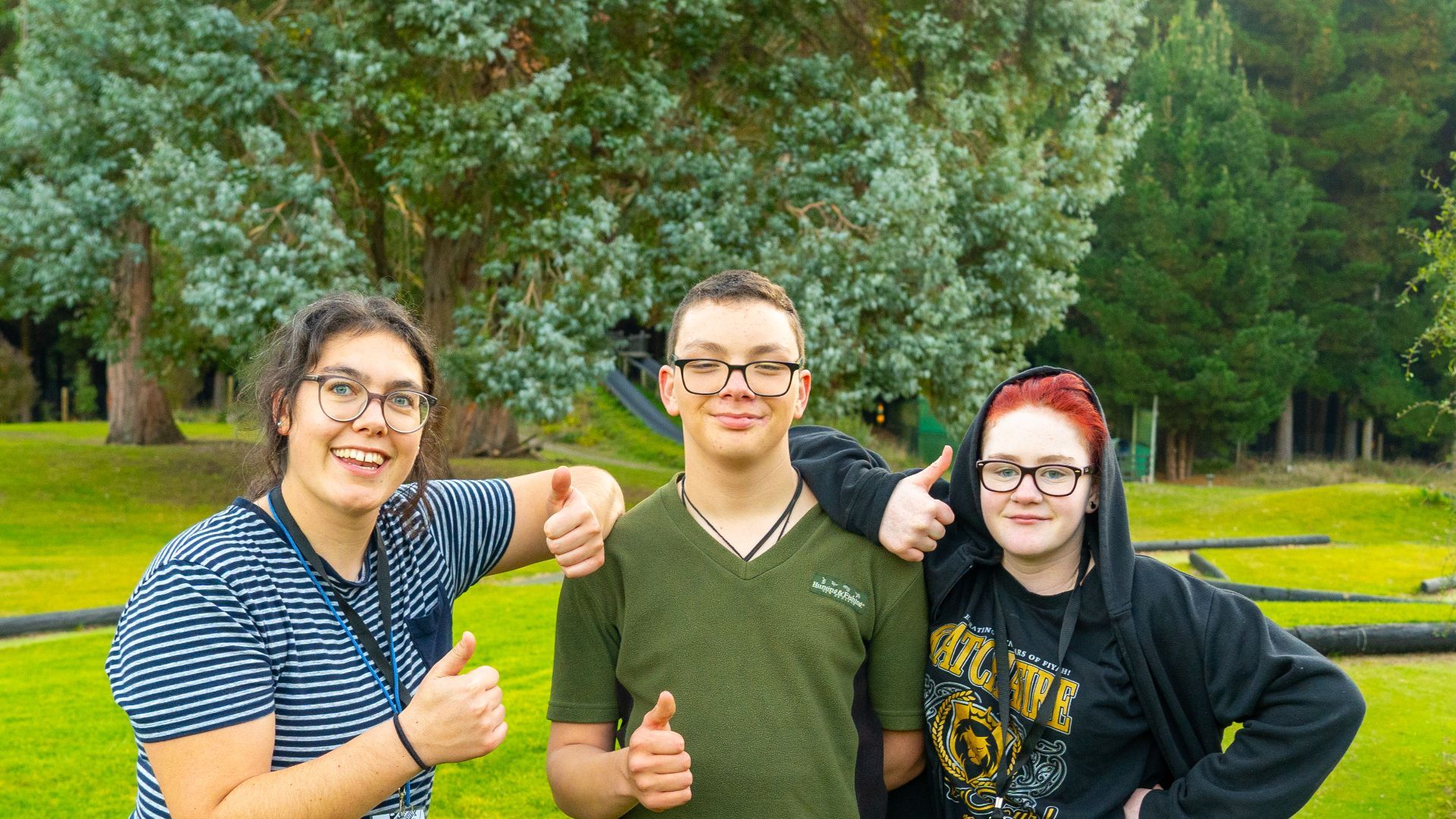 A group of young people are posing for a picture and giving a thumbs up.