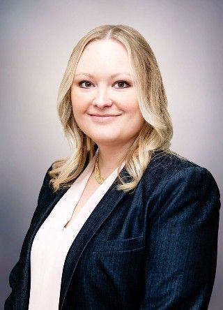 Woman with blonde hair, wearing a white top and navy blazer, smiling at the camera.