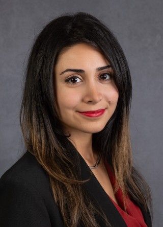 Woman in black blazer and red top, smiling, looking at camera.