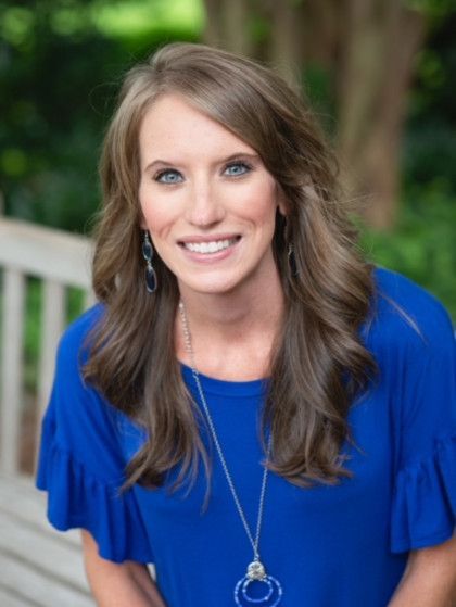 A woman in a blue shirt and necklace is sitting on a bench.