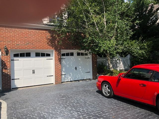 A red car is parked in front of a brick garage.