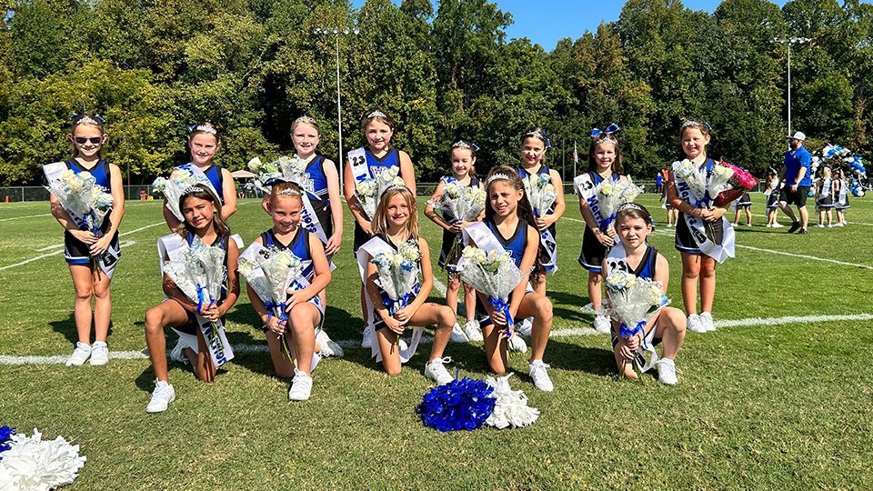 A group of cheerleaders are posing for a picture on a field.