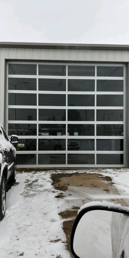 A car is parked in front of a garage door in the snow.