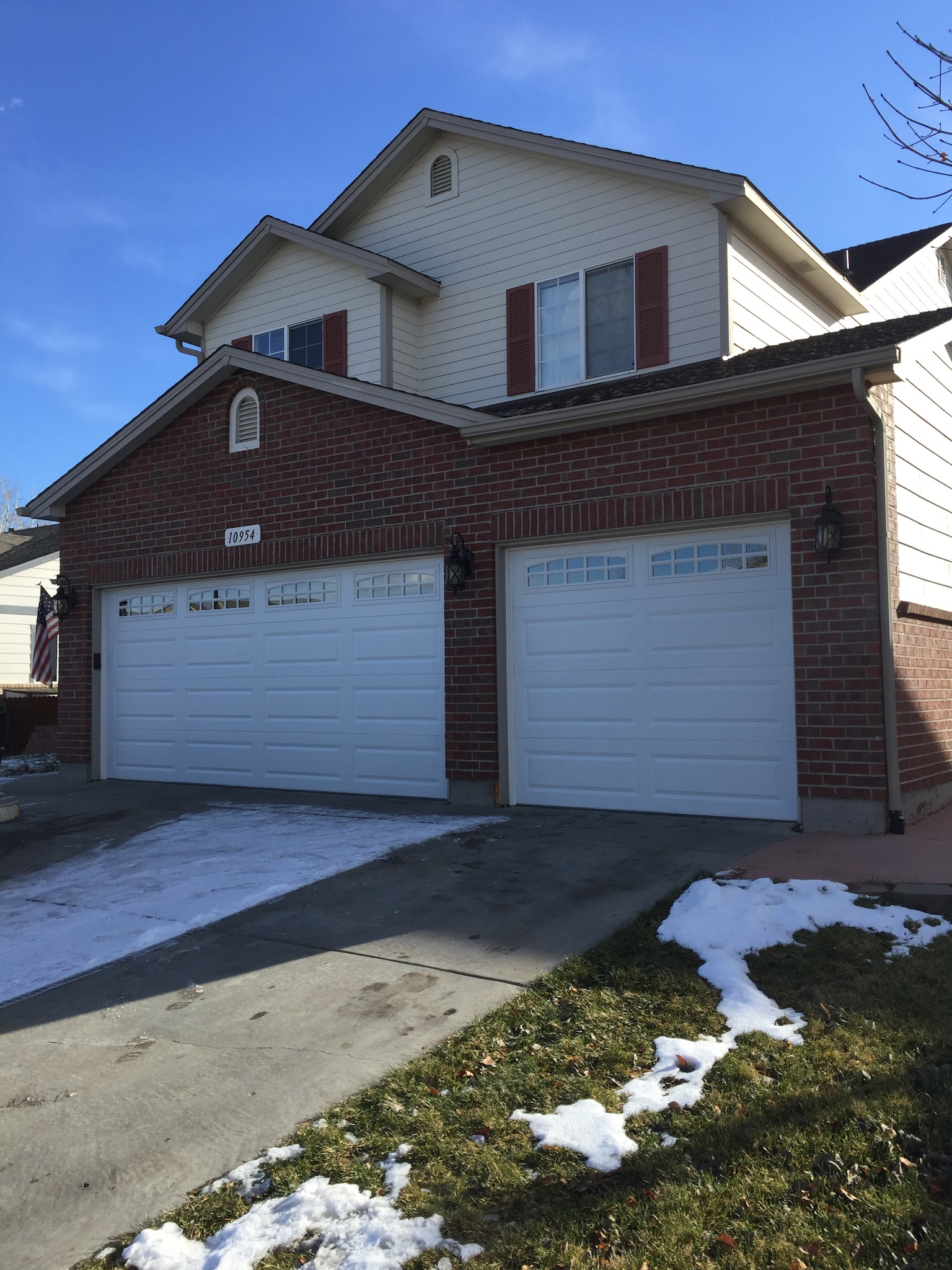 A large brick house with two white garage doors and snow on the ground.