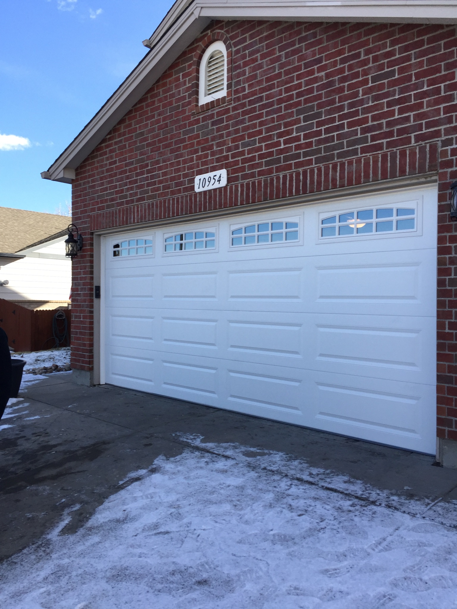 A man in a blue uniform is holding a tool bag in front of a garage door.
