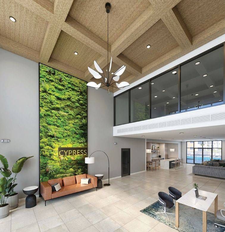 Modern lobby featuring a tall moss wall, a brown leather sofa, and a large chandelier under a coffered wood ceiling.