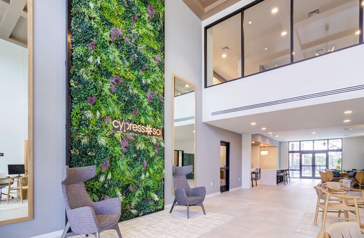 Bright modern lobby with a tall green plant wall, chairs, and a glass-railed mezzanine