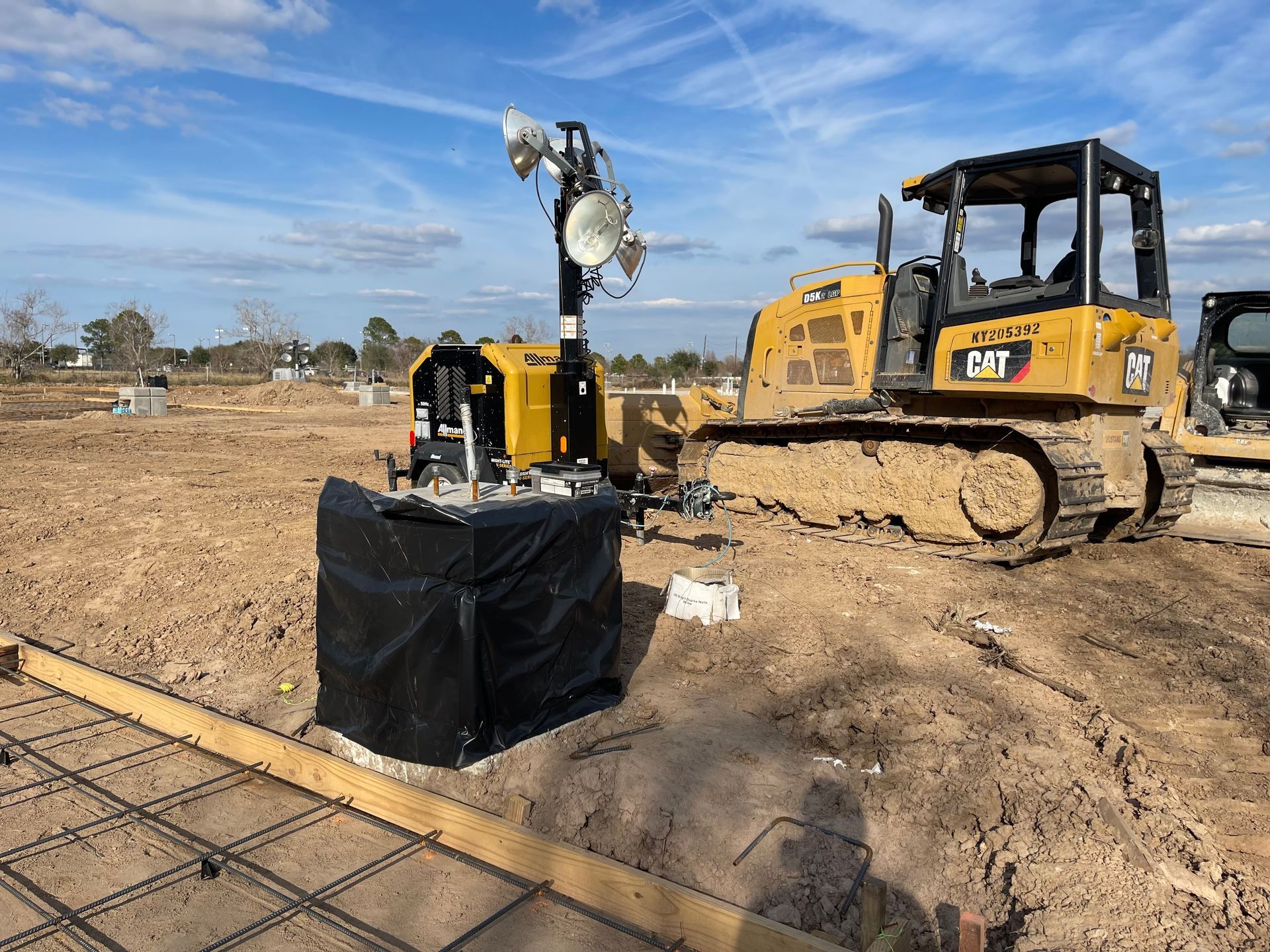 Yellow bulldozer and light tower at construction site, blue sky in background.