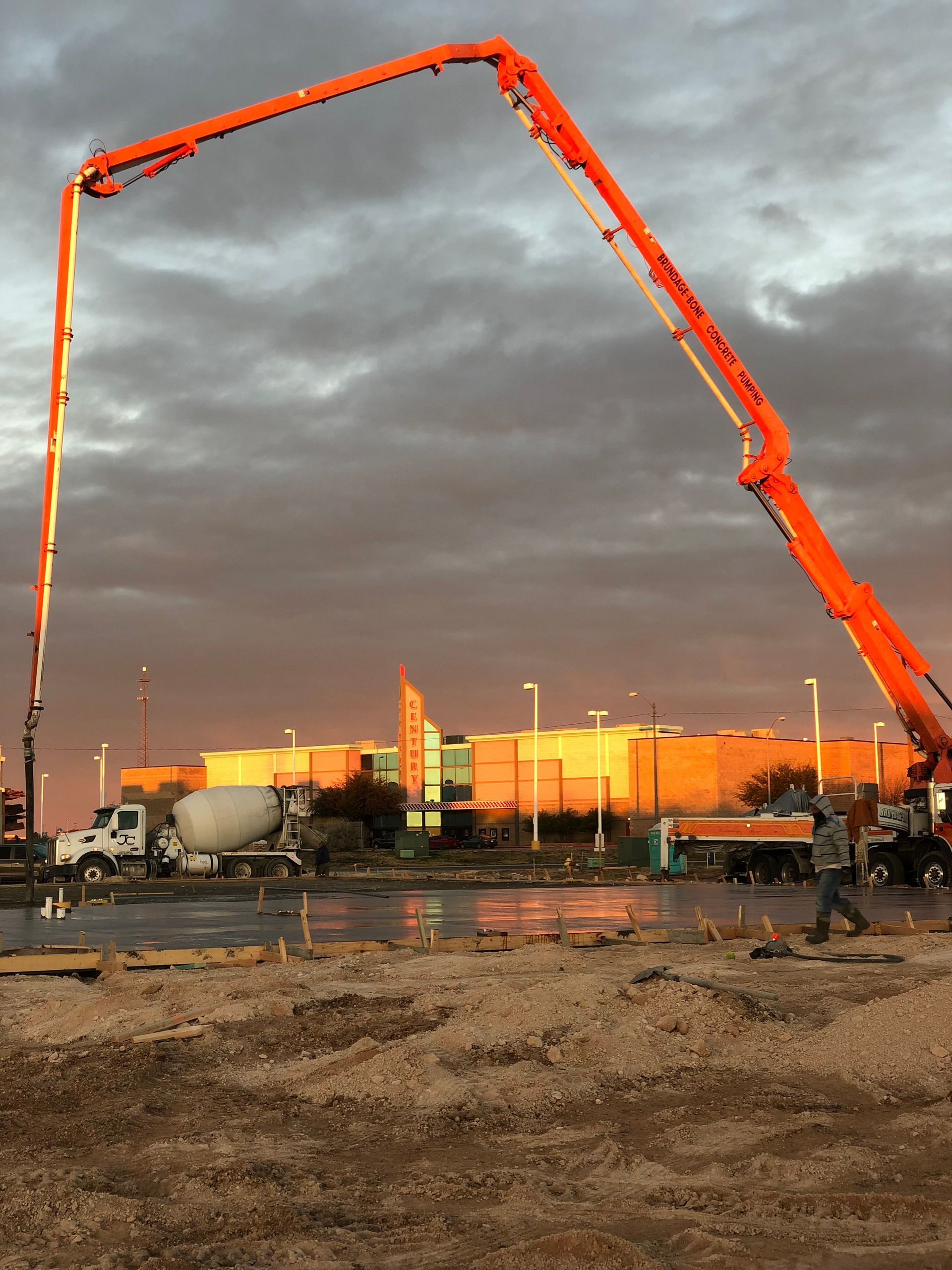 Orange concrete pump truck extending over a construction site at sunset.