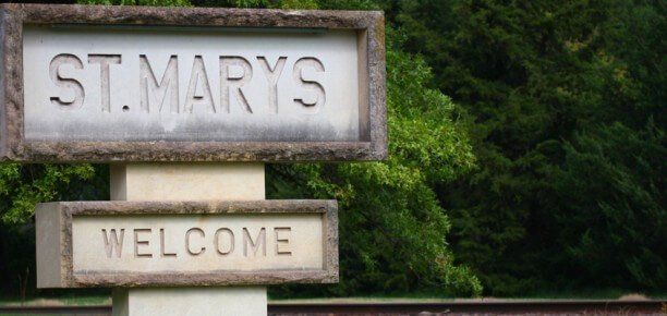 Wooden sign reading “ST. MARY’S” over “WELCOME” against green trees
