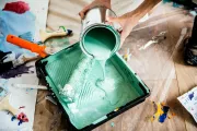 Pouring mint-green paint into a paint tray on a messy worktable with brushes and supplies