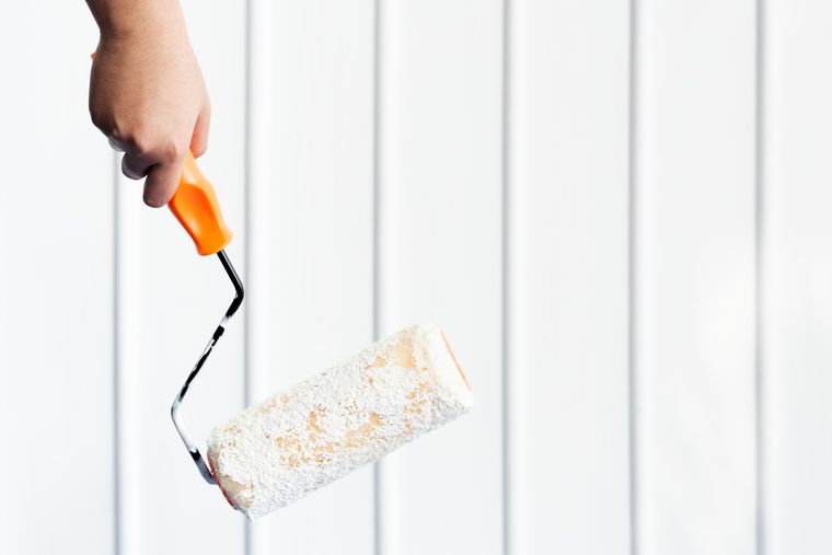 Hand using a paint roller to coat a white wall with orange paint