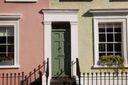 Row of pastel townhouses with a green front door and white-trimmed windows behind black iron railings