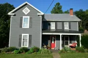 Gray two-story house with white trim, red door, and front porch in a sunny yard
