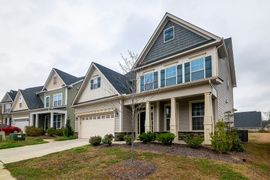 Row of new suburban houses with beige siding, stone accents, and attached garages under an overcast sky
