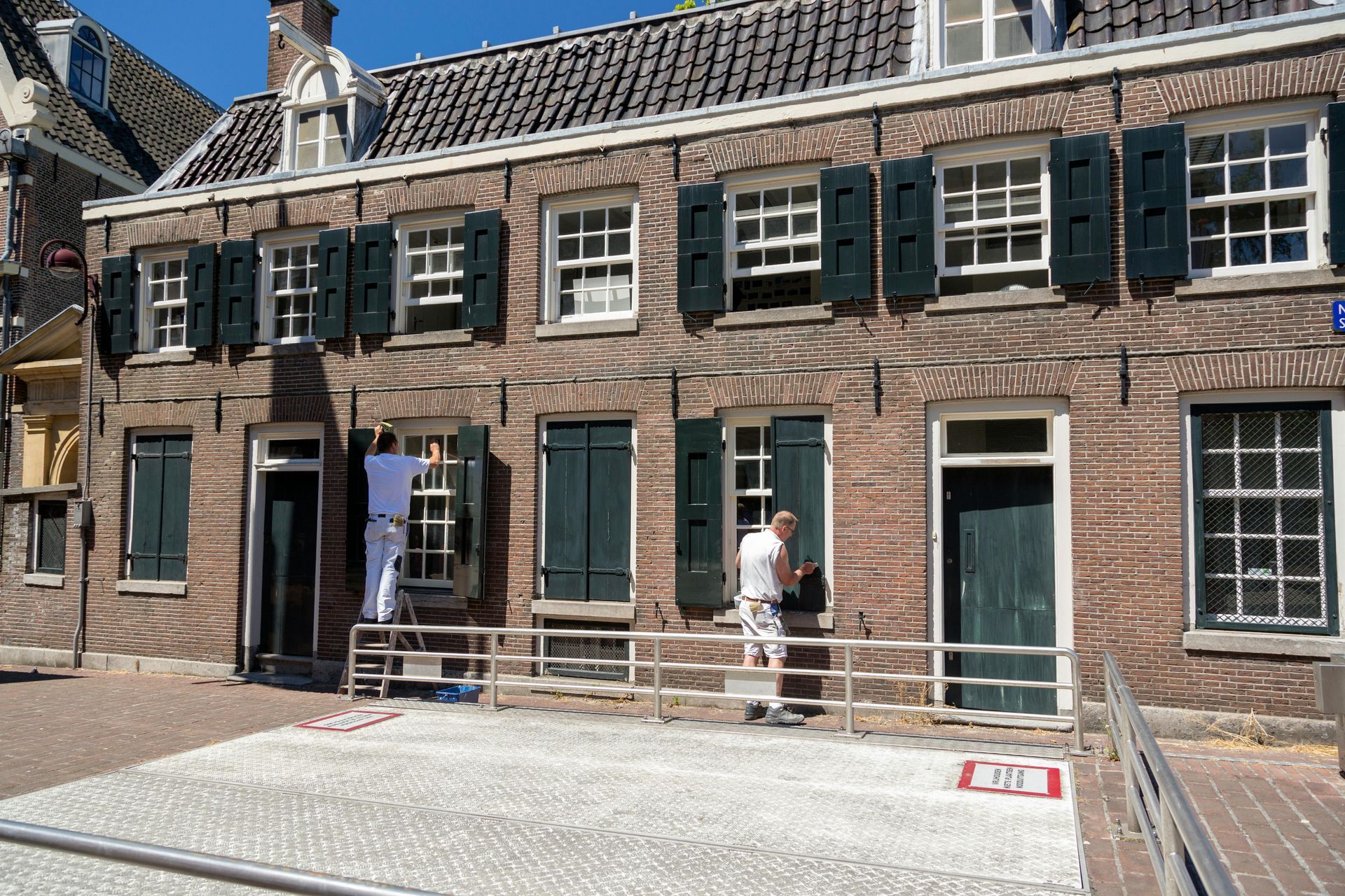 Historic brick building with dark shutters and people on scaffolding in a courtyard