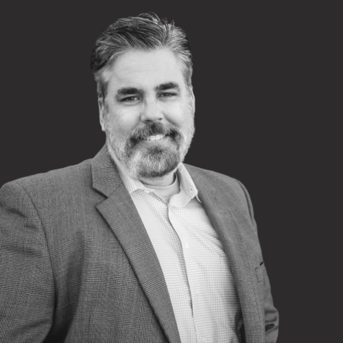 A man with a beard is wearing a suit and smiling in a black and white photo.