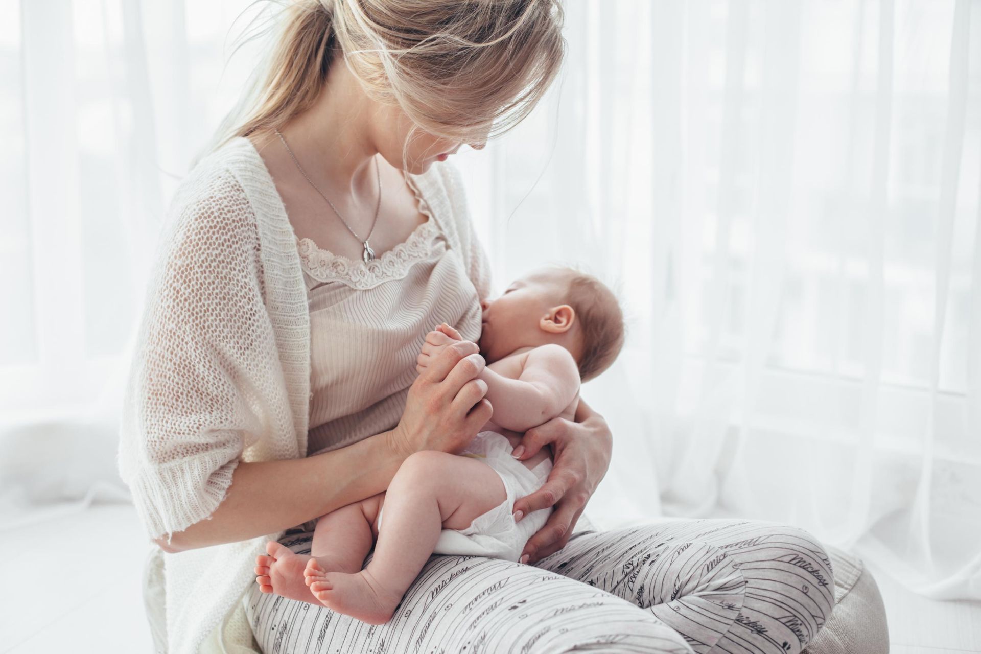 Person cradling a baby by a bright window, both in soft white clothing