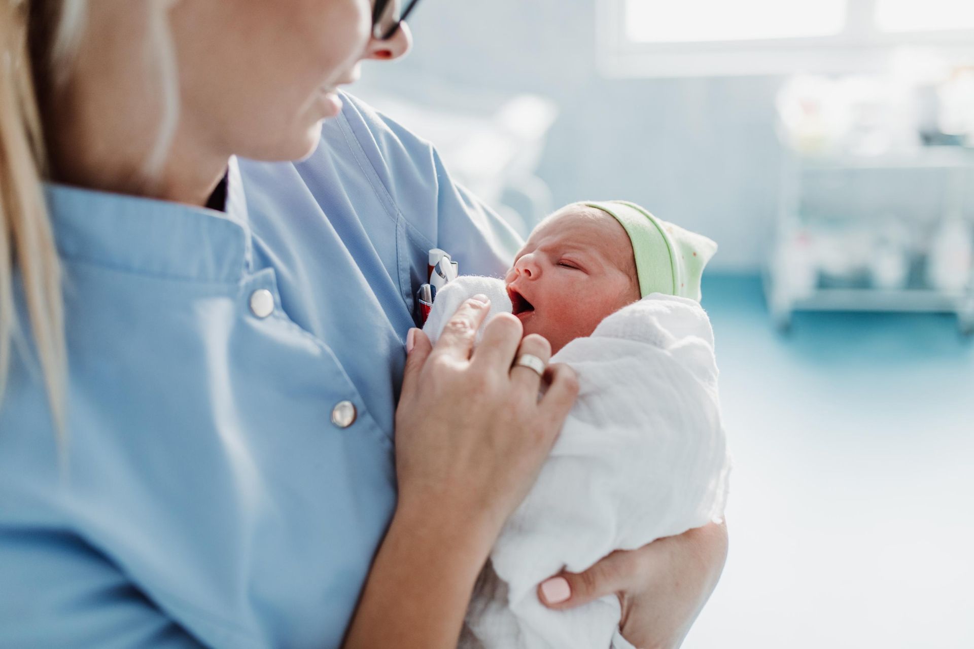 Nurse gently holding and checking a swaddled newborn in a hospital setting