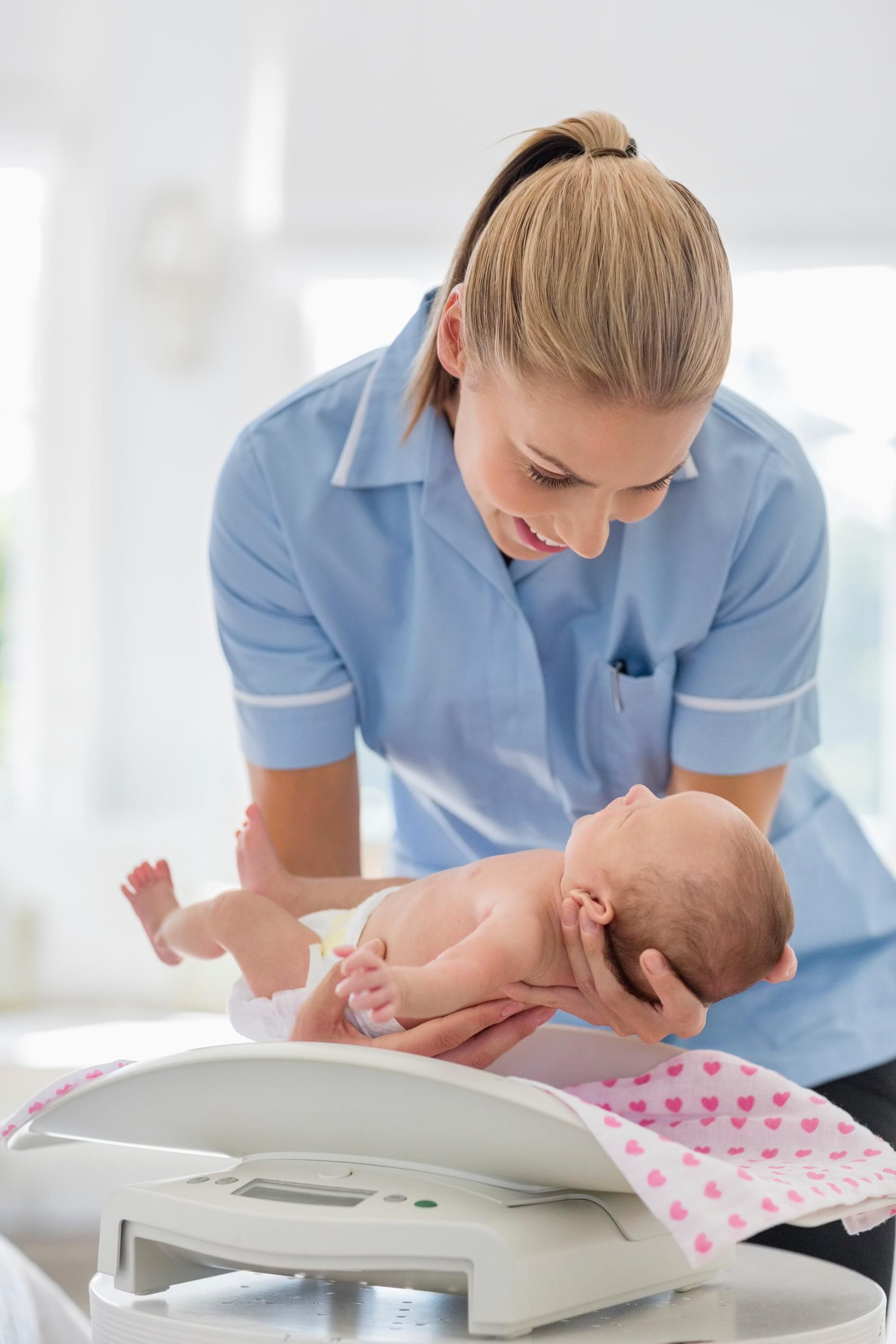 Nurse gently examines a newborn on a changing table in a bright clinic room