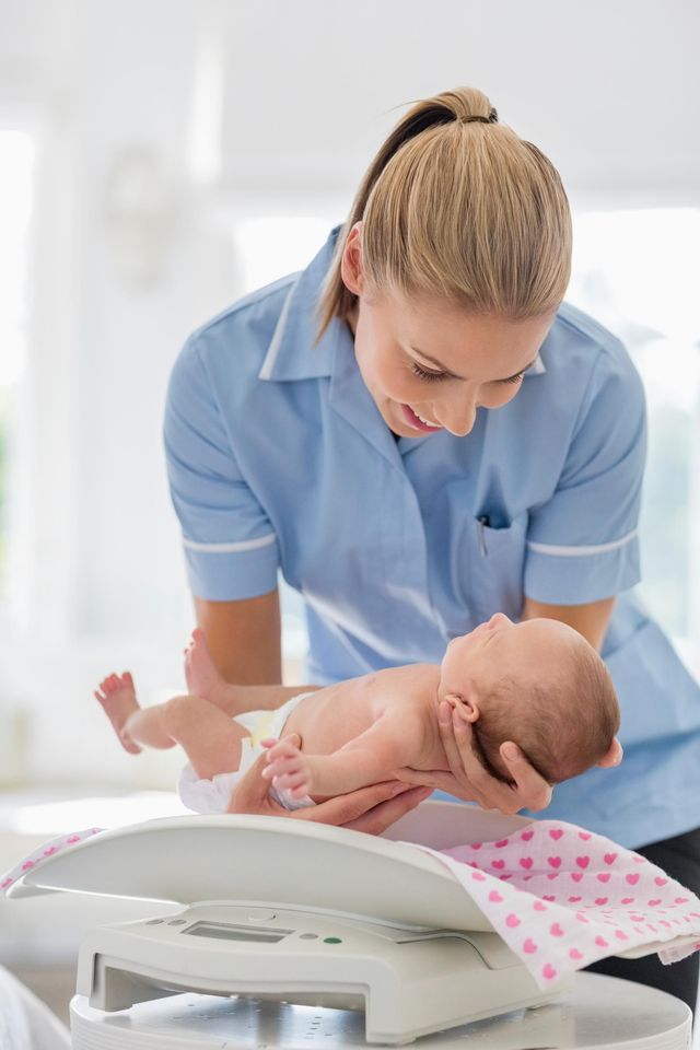 Nurse in blue uniform weighing a baby on a scale in a bright clinic