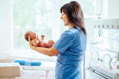 Nurse holding a newborn in a bright neonatal hospital room