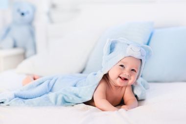 Smiling baby in a blue bear costume lying on a white bed