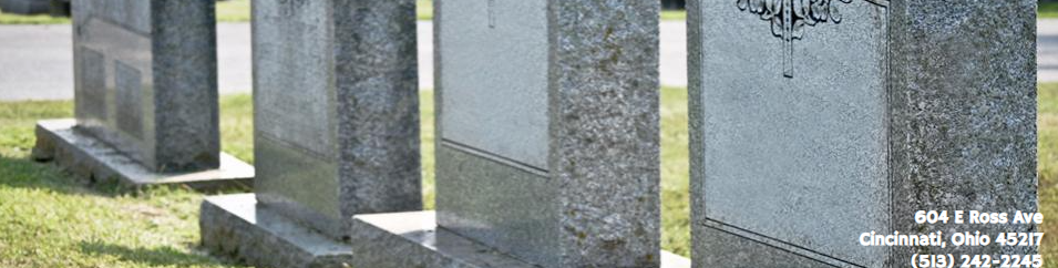Rows of upright gray granite gravestones in a green cemetery under bright sunlight.