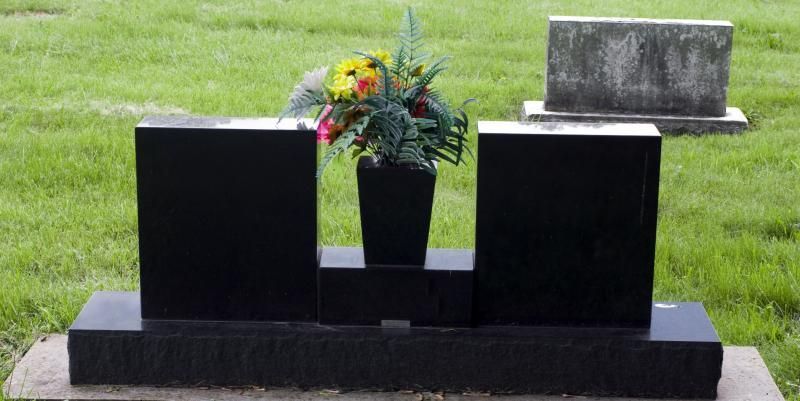 Black granite gravestone with flower vase in a grassy cemetery