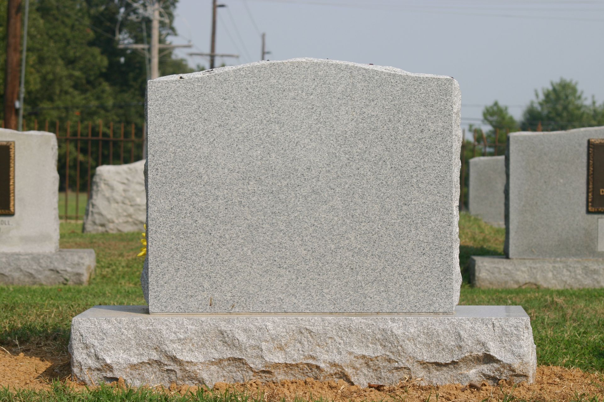 Gray granite headstone in a cemetery, with grass and other gravestones in the background.