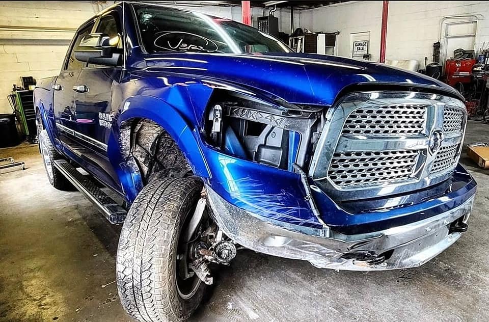 A blue ram truck with a damaged front end is parked in a garage.